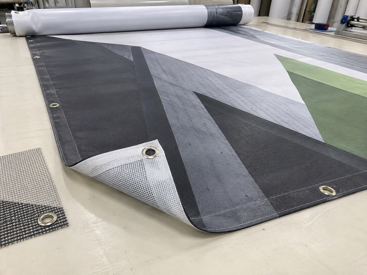 Printed PVC advertising banner with hem and metal eyelets beside a mesh sample